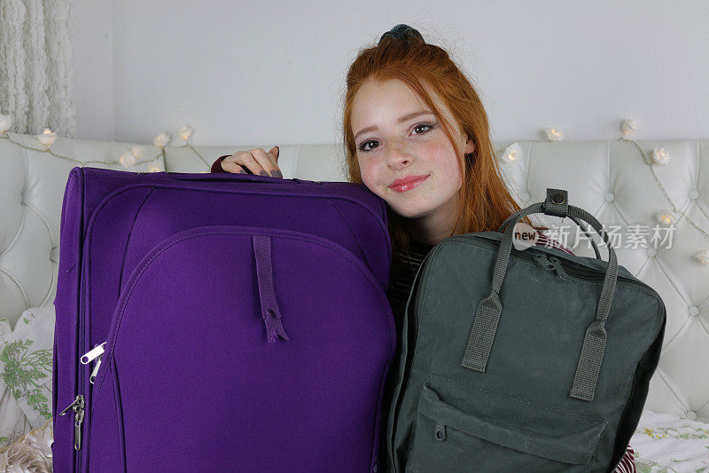 红色头发的少女14 / 15举着她的旅行行李，紫色的行李箱和旅行包，期待着度假